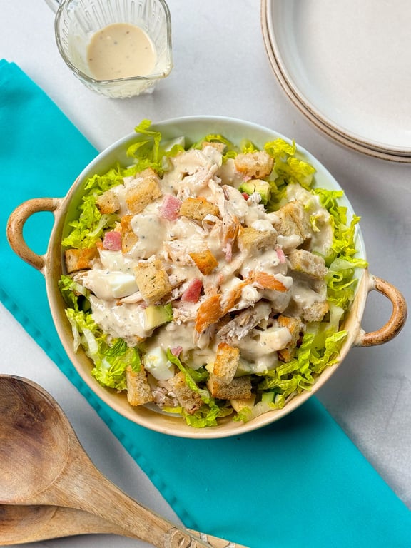 Bowl of Caesar salad with lettuce, croutons, chicken, ham, and creamy dressing