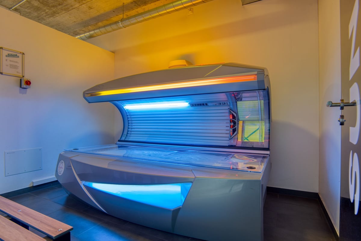 PureGym Lenzburg : Un lit de bronzage à éclairage bleu se trouve dans une pièce aux murs et au plafond jaunes.