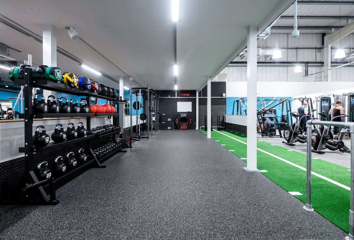 PureGym Folkestone: Free weight racks, medicine balls, rubberized flooring, green turf area, and strength machines.