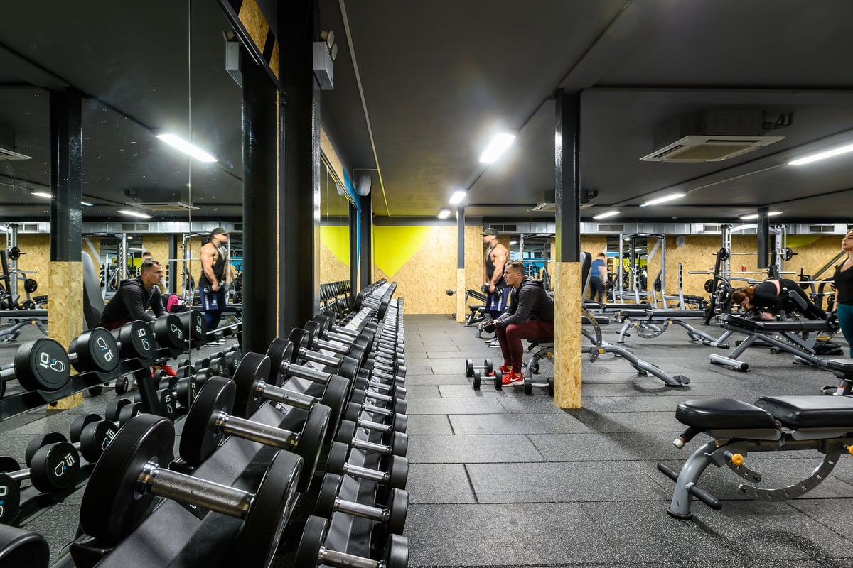 PureGym Reading Caversham Road: Rows of dumbbell racks, weight benches, and exercise equipment in a dimly lit gym setting.