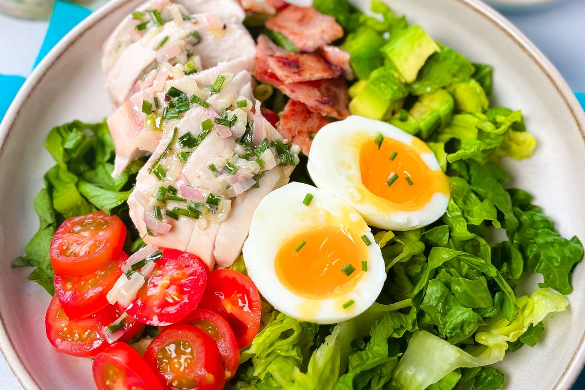 Bowl of salad with sliced boiled eggs, cooked chicken, bacon, avocado and tomatoes