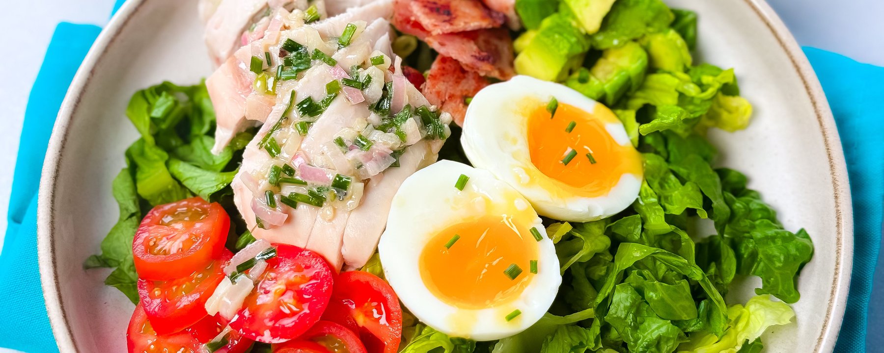 Bowl of salad with sliced boiled eggs, cooked chicken, bacon, avocado and tomatoes