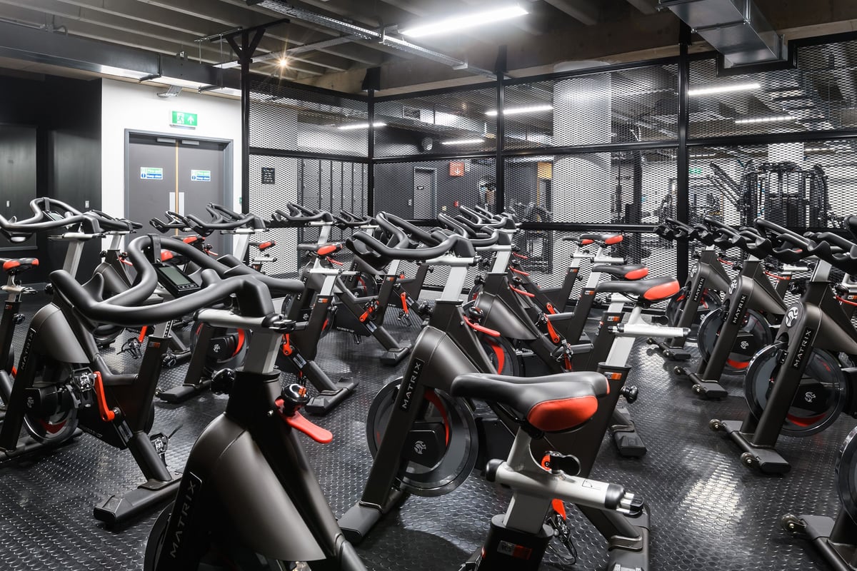 PureGym Birmingham Arcadian Centre: Rows of stationary bikes inside a dimly lit gym studio with industrial ceiling ducts.