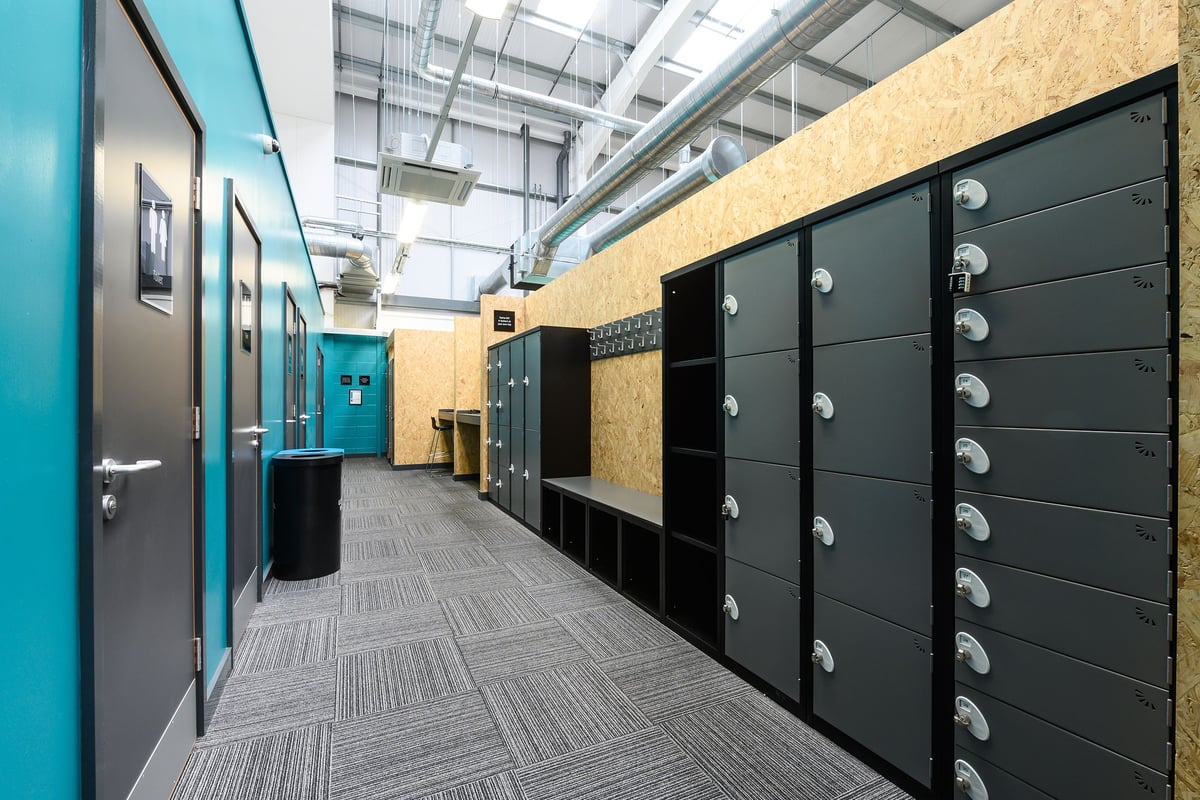 PureGym Saffron Walden: Rows of lockers, benches along the corridor, and tiled flooring.