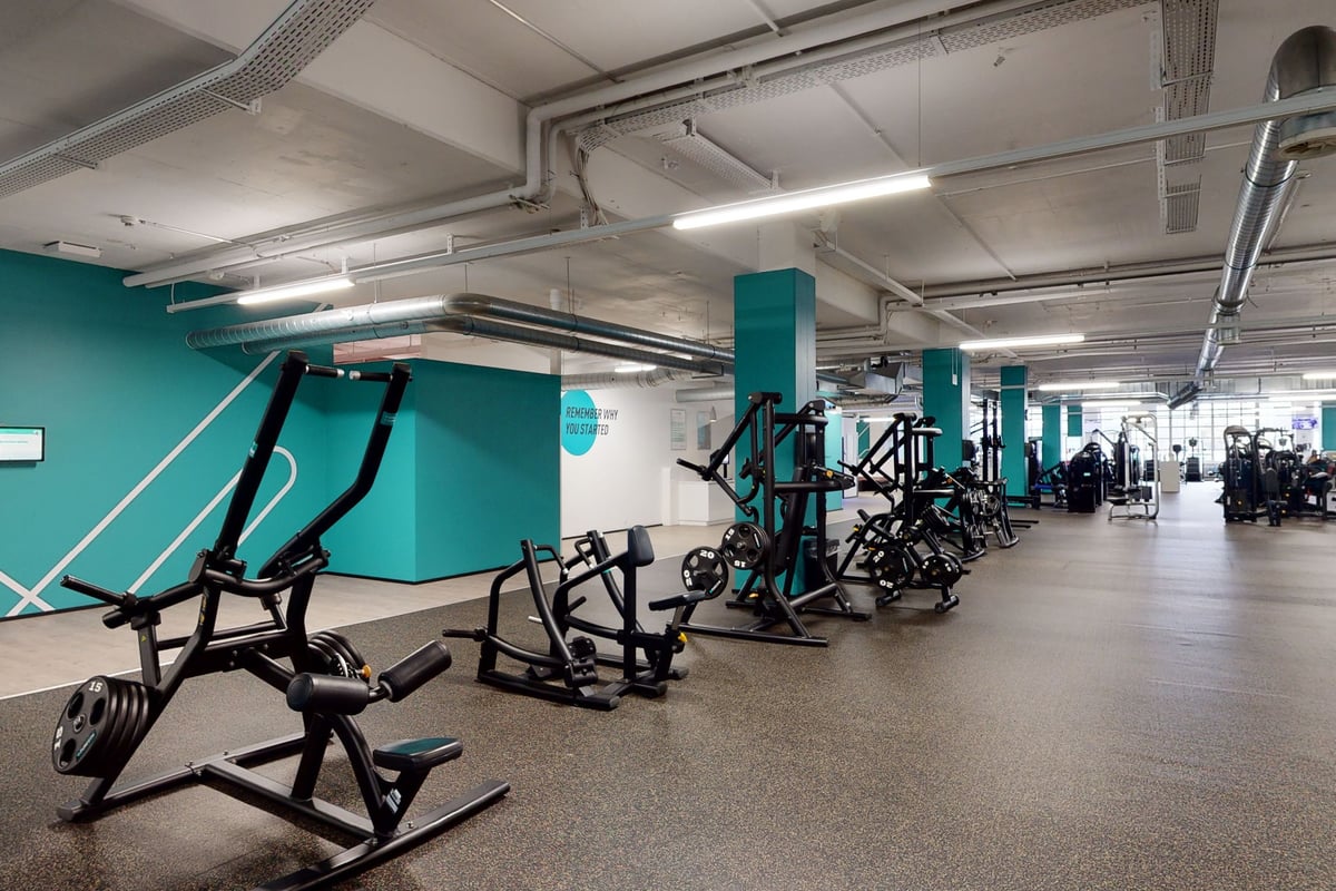 PureGym Bern Bümpliz: Salle de sport avec appareils de musculation, bancs, sols caoutchoutés et murs d'accent bleu sarcelle.