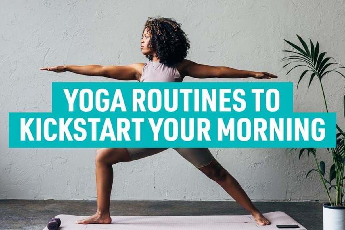 Woman in workout clothes doing yoga pose on mat beside potted plant against grey wall