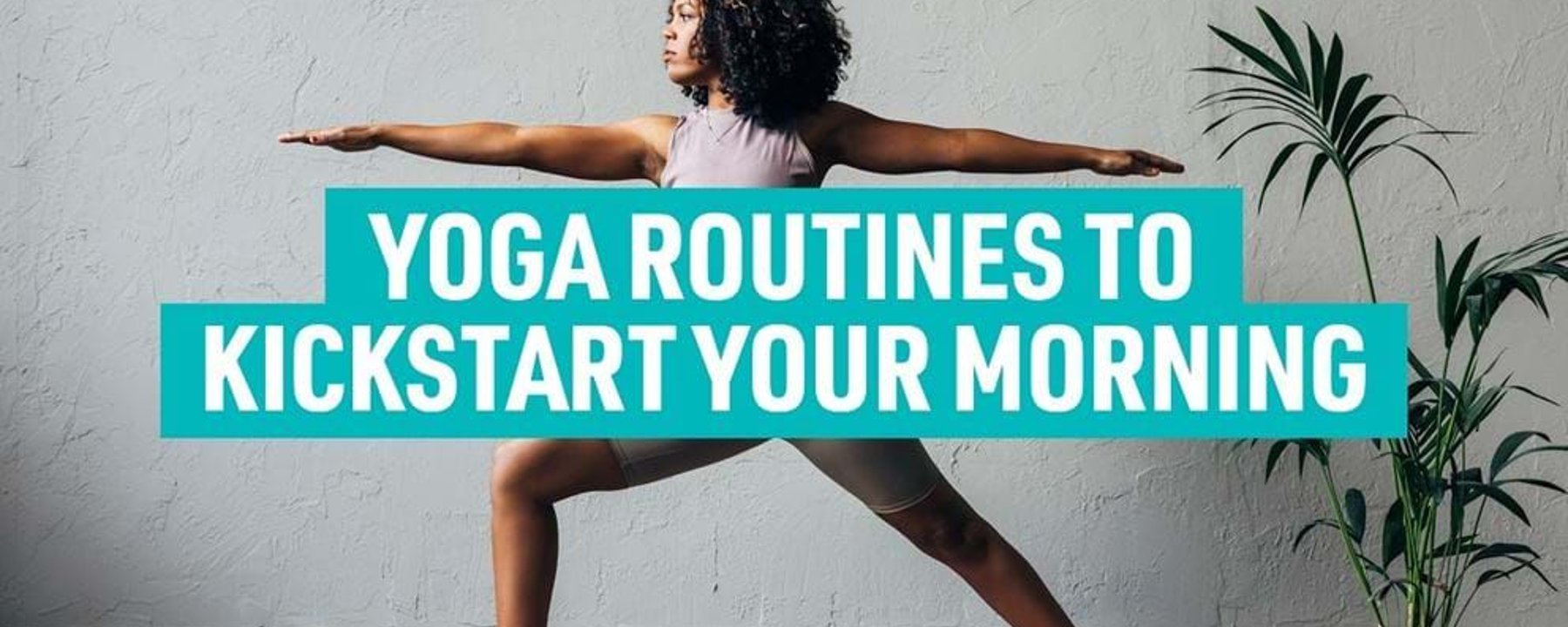 Woman in workout clothes doing yoga pose on mat beside potted plant against grey wall