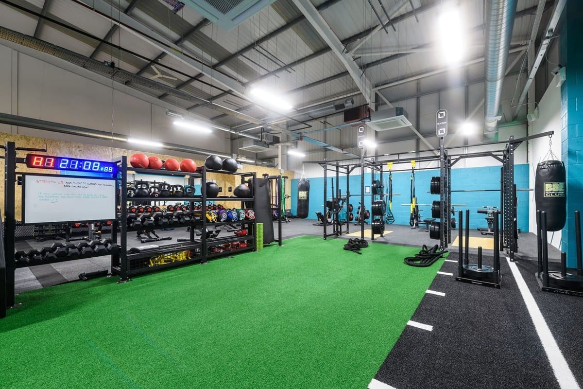 PureGym Buckingham: Gym with weightlifting racks, dumbbells, punching bags, turf area, weight plates, and digital timers.