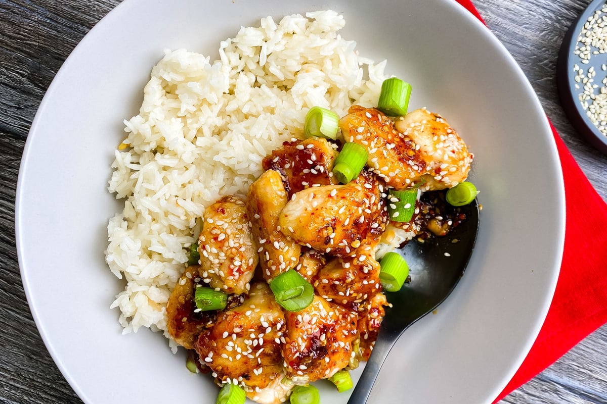 Glazed chicken pieces with sesame seeds and spring onions served with white rice
