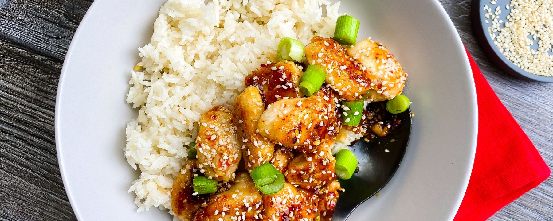 Glazed chicken pieces with sesame seeds and spring onions served with white rice