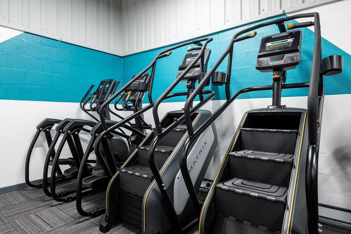 PureGym Alfreton: Rows of exercise bikes with screens facing a mirrored wall in a teal-colored gym studio.