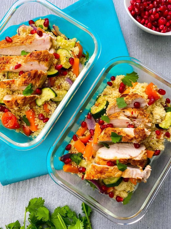 Grilled chicken slices on couscous with vegetables and pomegranate seeds in glass container