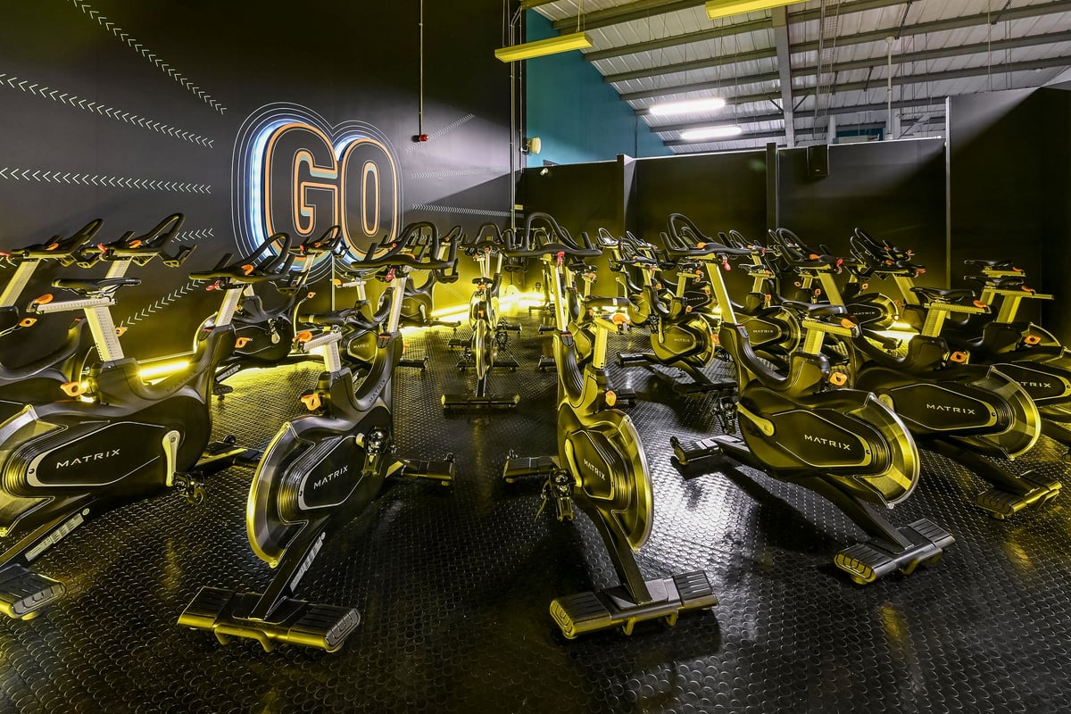 PureGym Canterbury Sturry Road: Rows of stationary bikes with "GO" neon sign illuminating the darkened studio interior.