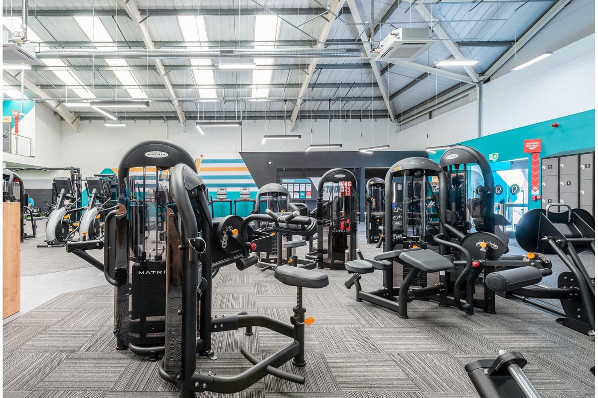 PureGym Cannock Orbital Retail Park: Gym with weight machines, benches, rubberized flooring, and teal accents on the walls.