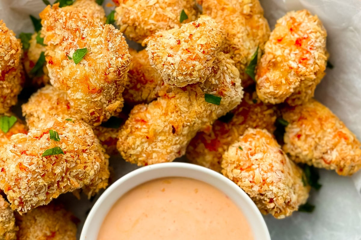 Golden breaded chicken pieces with red chilli flakes and a bowl of pink dipping sauce