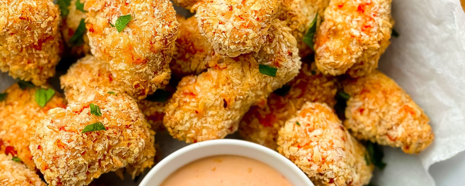 Golden breaded chicken pieces with red chilli flakes and a bowl of pink dipping sauce