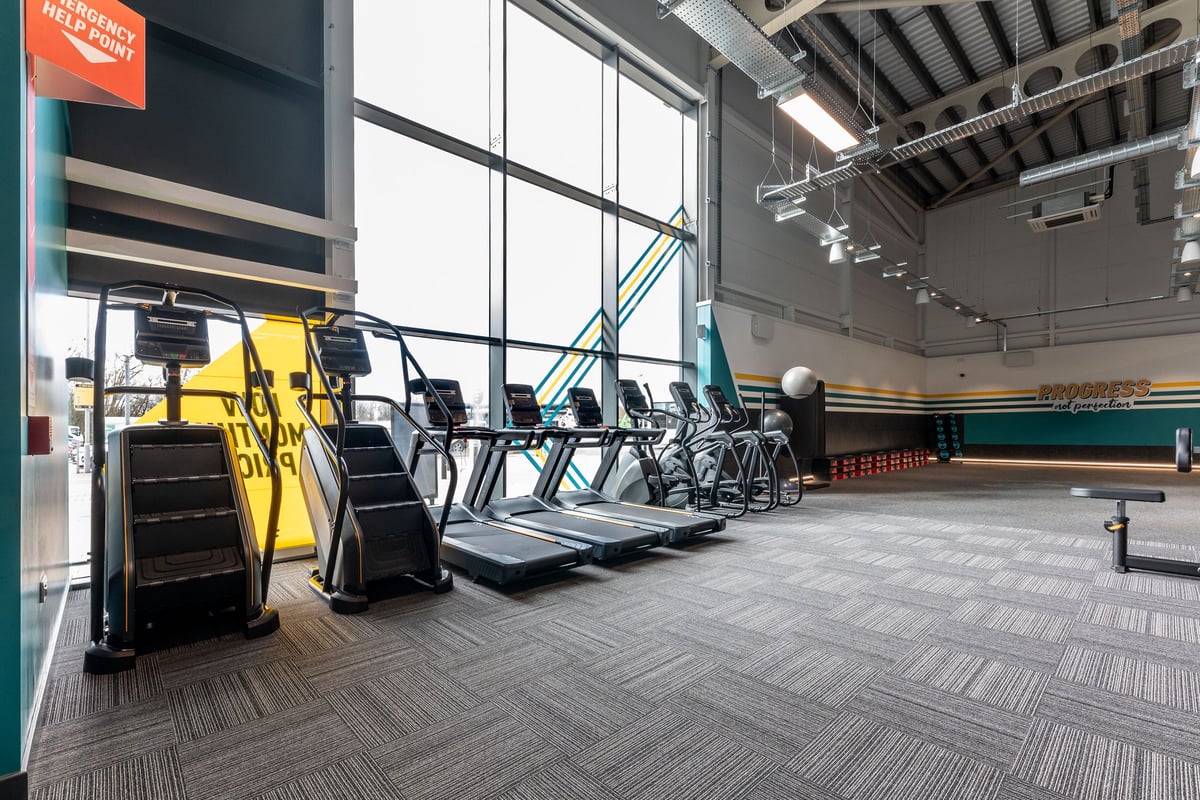 PureGym St Ives Cambridgeshire: Rows of treadmills, ellipticals, and weight machines in a modern gym with large windows.