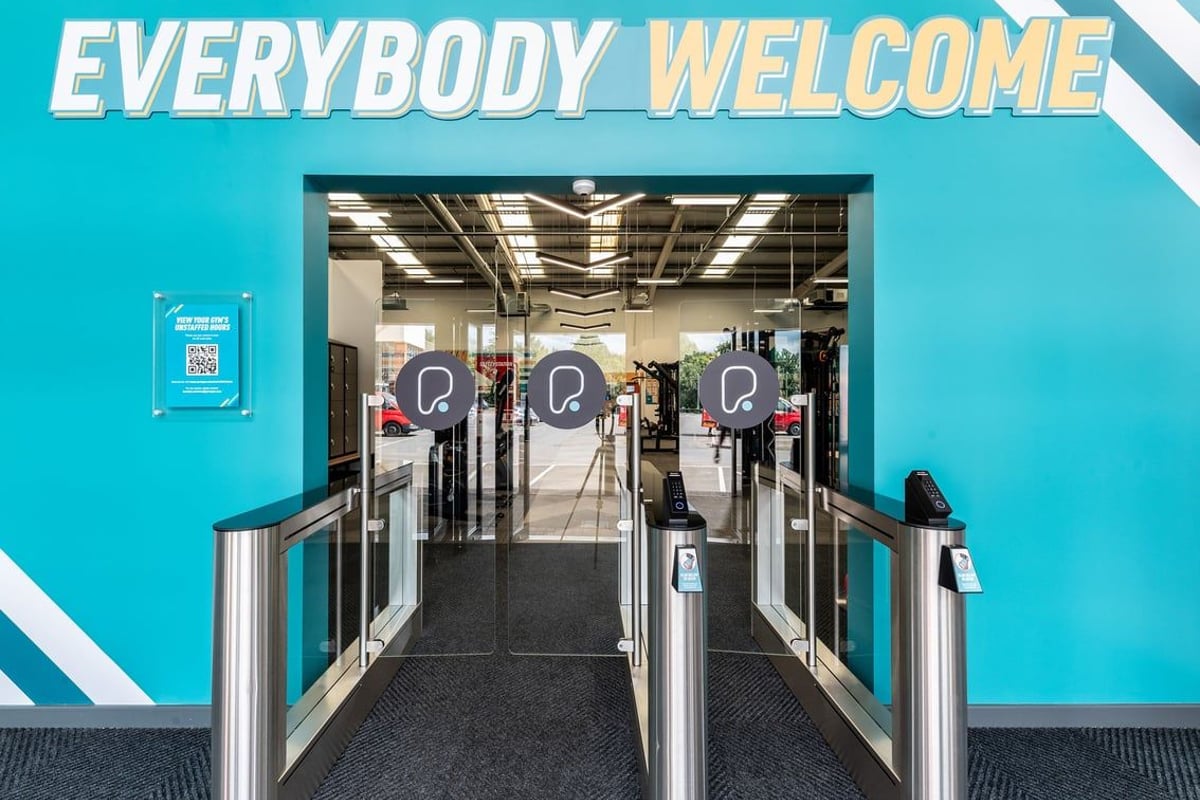 PureGym Dumfries: Turnstiles, corridor leading inside with minimalist decor and signage saying "Everybody Welcome".