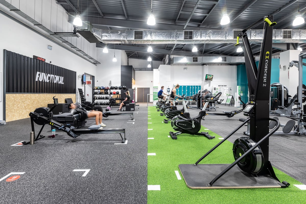 PureGym Warrington Central: Functional training area with turf, plate-loaded machines, squat racks, rubberized flooring.