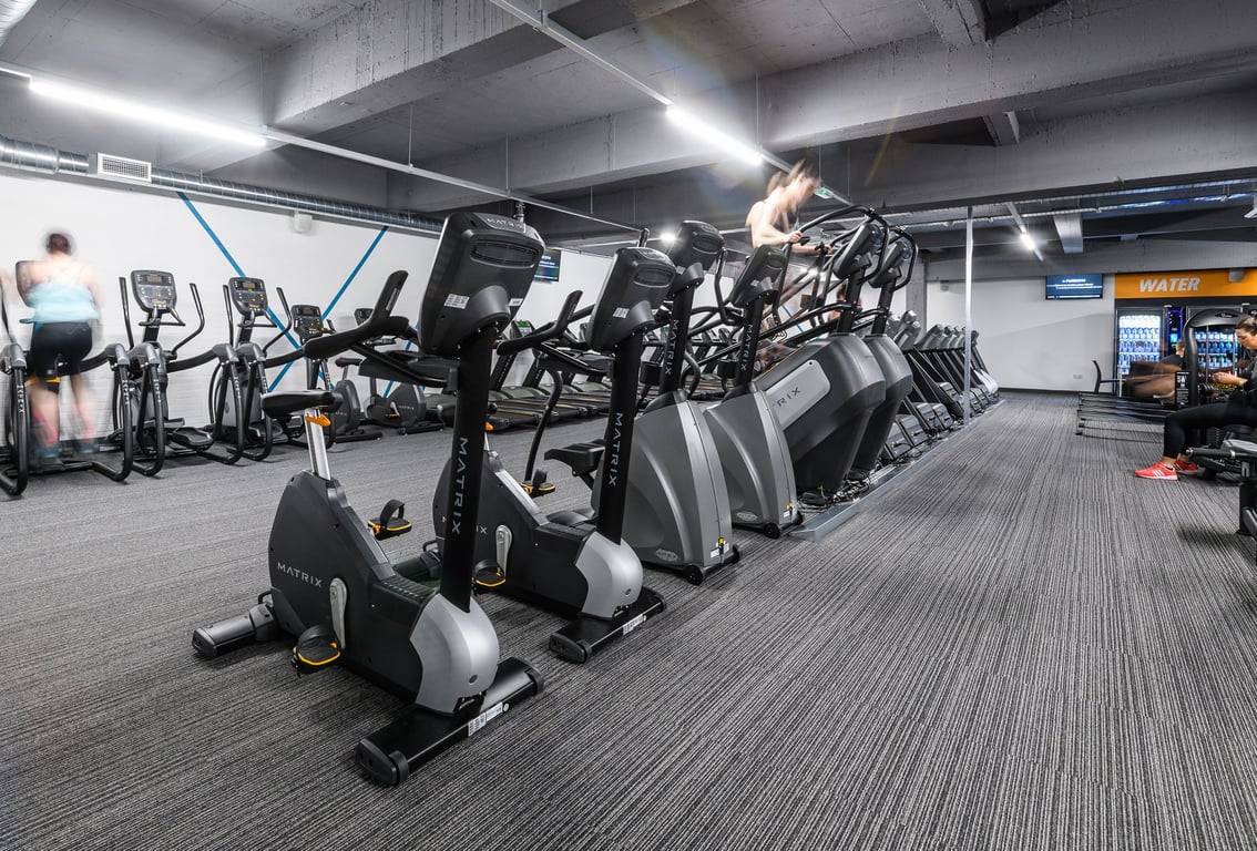 PureGym Exeter Fore Street: Rows of stationary bikes, ellipticals, and treadmills in a dimly lit gym space.