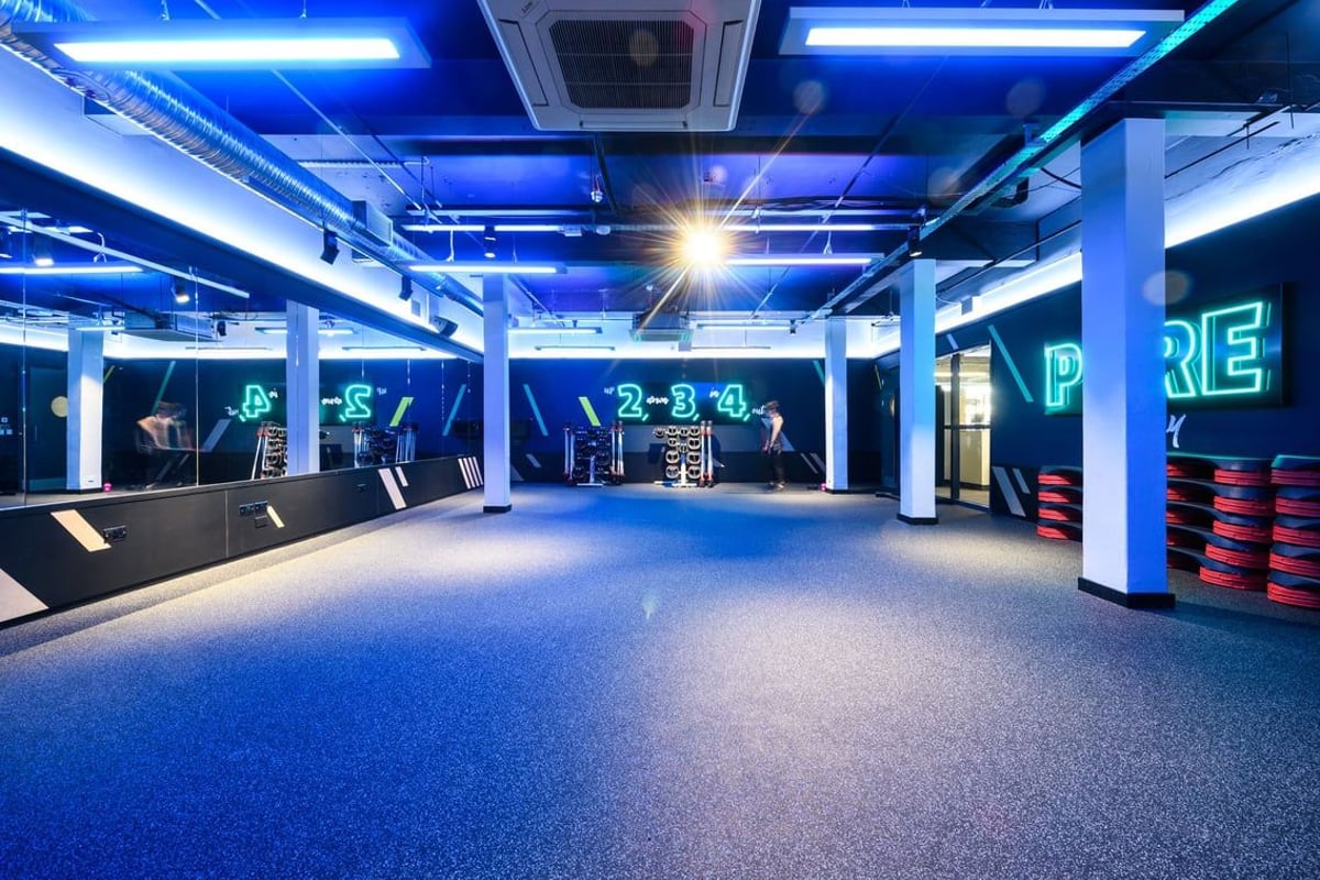 PureGym London Camden: Spacious gym studio with exercise rigs, padding, mirrors, and neon blue lighting.