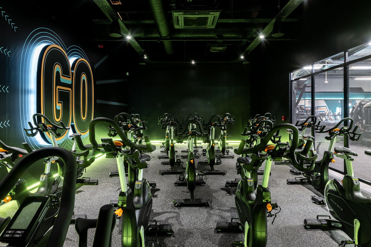 PureGym Aintree: Rows of stationary bikes, neon green lighting, and a large "GO" sign.