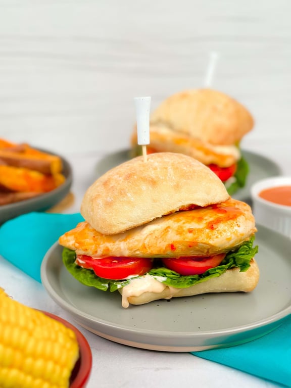 Grilled chicken sandwich with lettuce and tomato on a grey plate with a blue napkin.