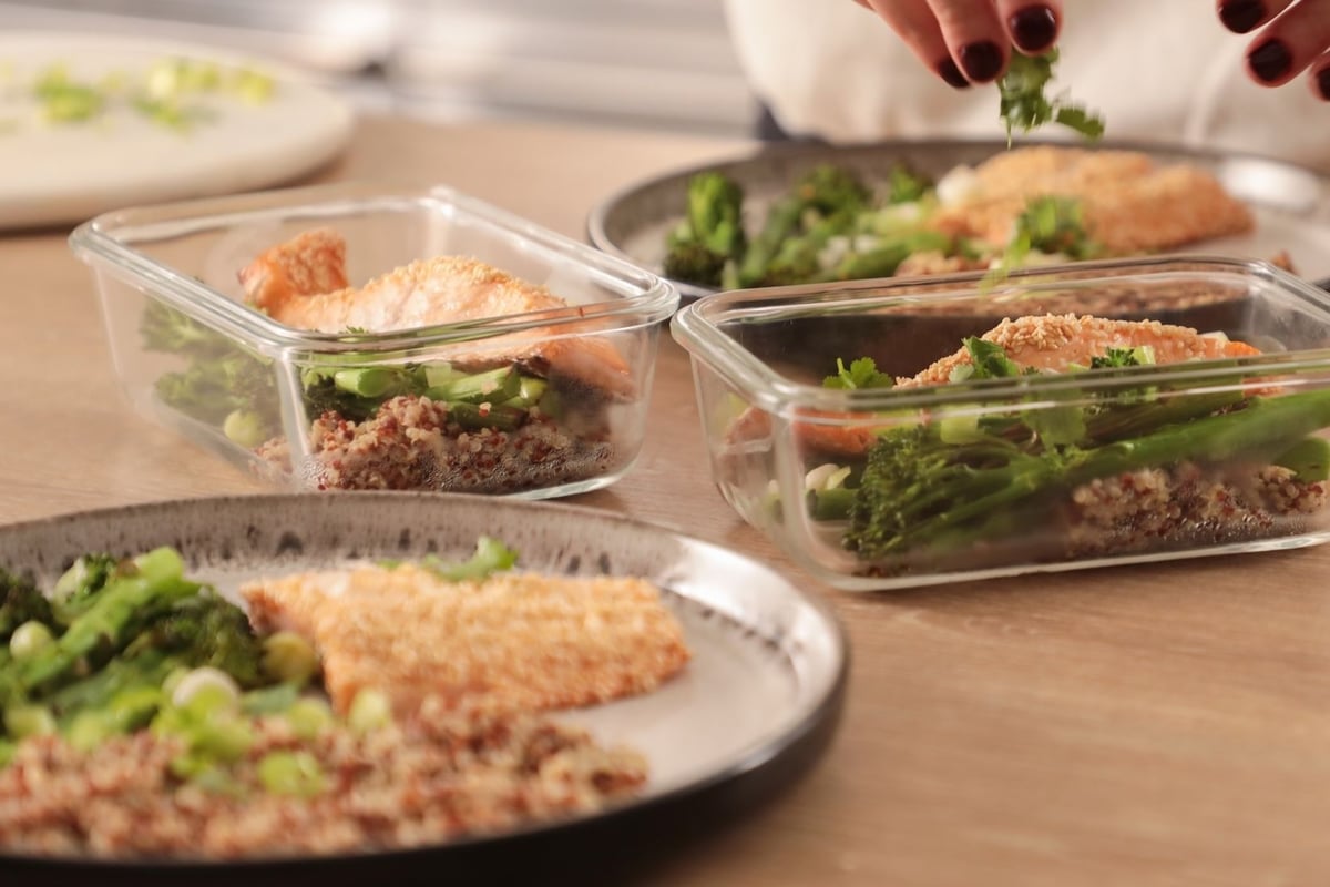 Person garnishing meal prep containers with broccoli, quinoa and salmon