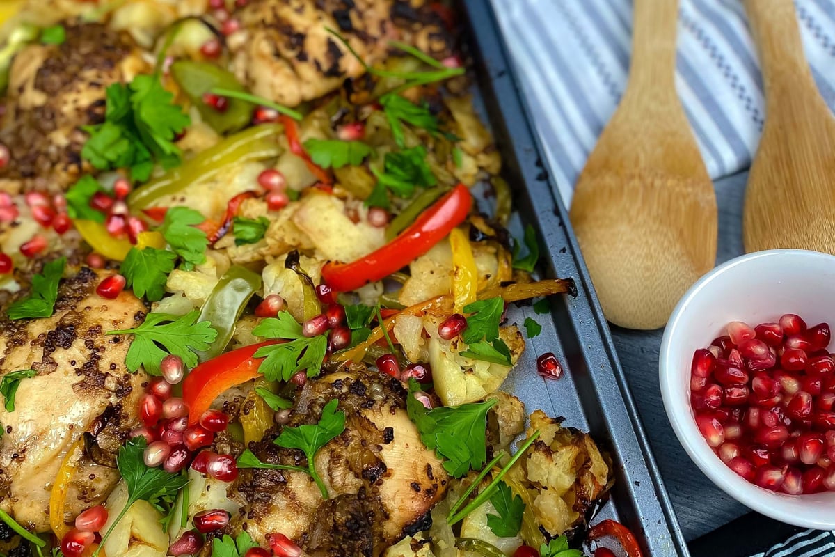 Tray of roasted chicken with mixed peppers, cauliflower, parsley, and pomegranate seeds