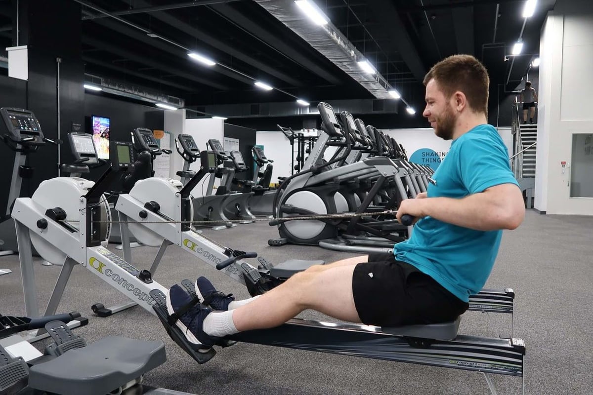 Man in blue shirt using rowing machine in gym with exercise bikes and treadmills nearby