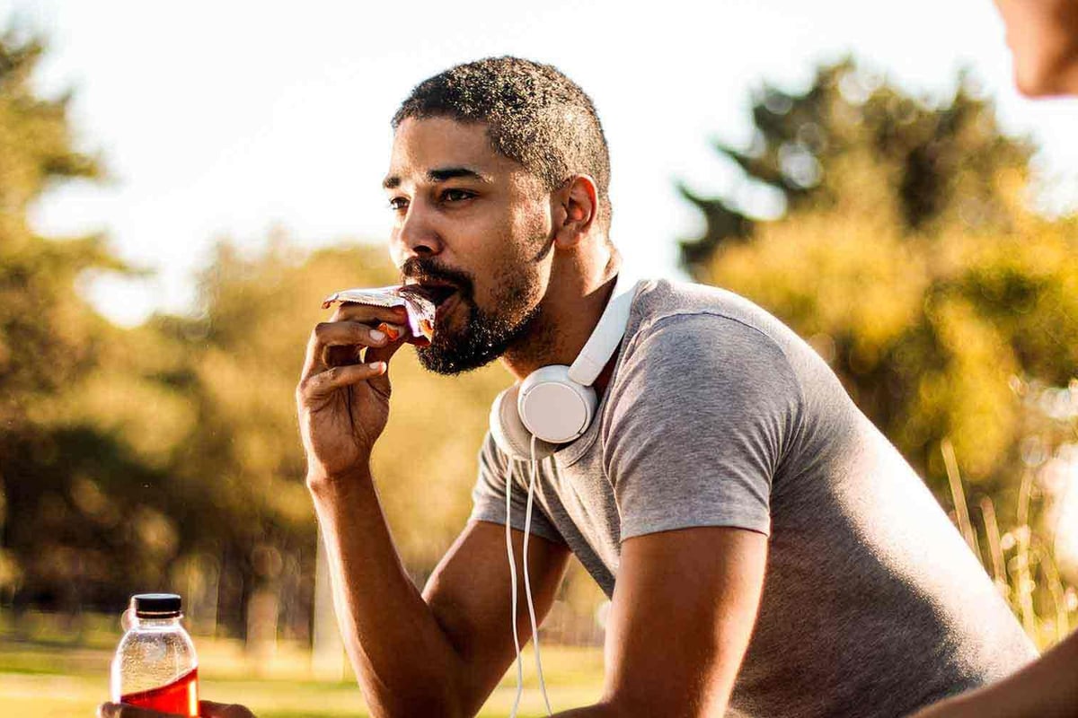 Mann mit Kopfhörern isst Snack im Park und spricht mit einer anderen Person.