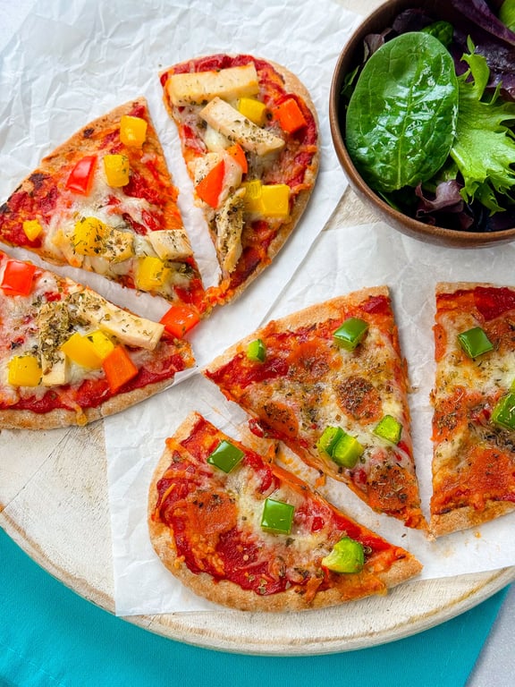 Slices of vegetable pizza with green salad in a wooden bowl on a round board