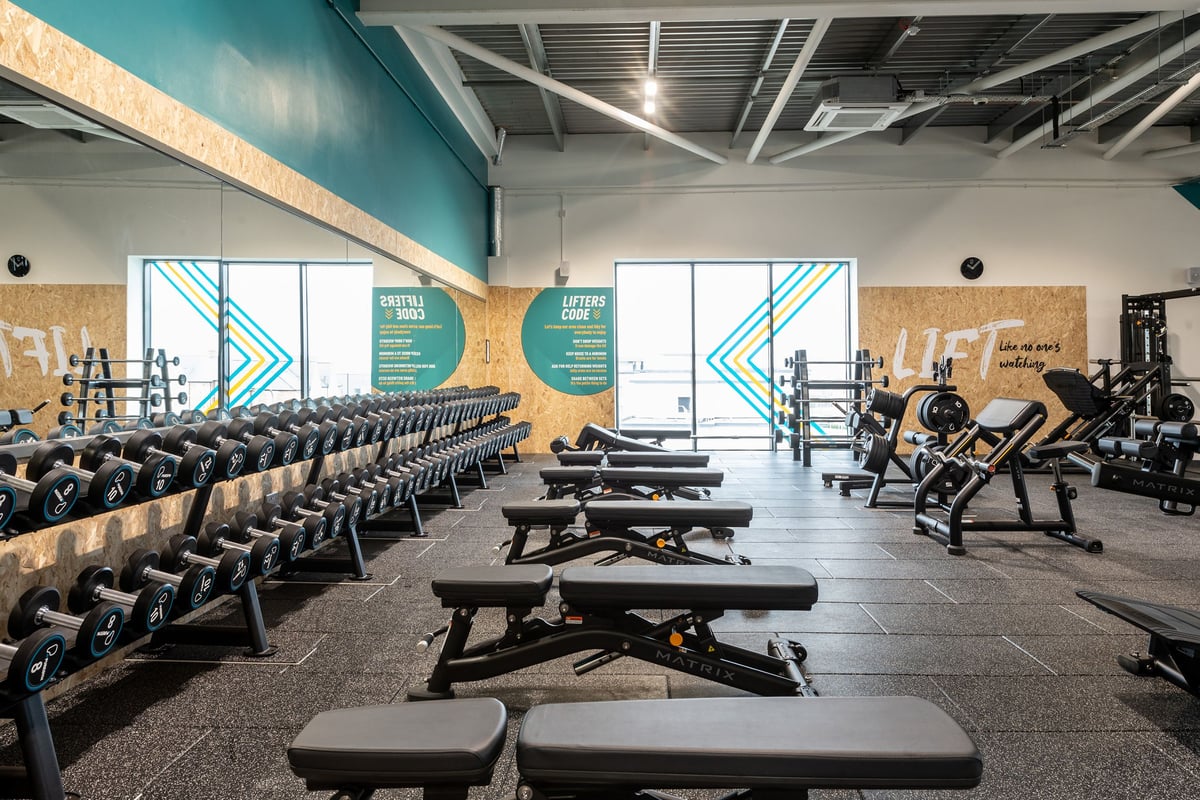 PureGym Bicester: Rows of dumbbell racks, benches, weight plates, and mirrored walls in a gym studio.