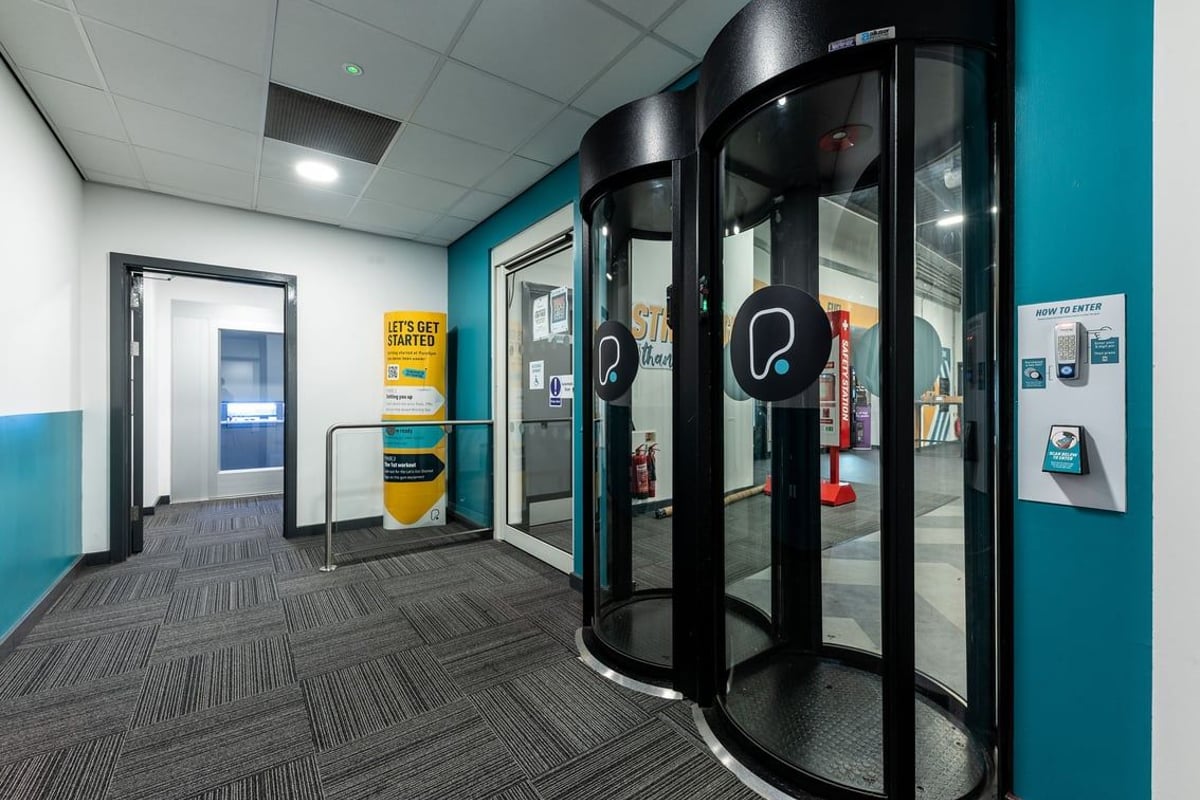 PureGym Chatham: Revolving doors, vending machines, wall adverts in a gym entry or lobby area.