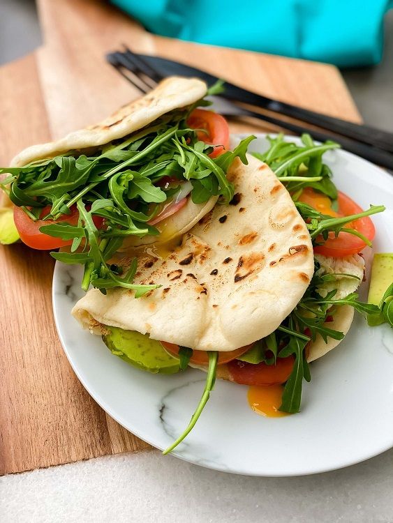 Flatbread sandwiches filled with arugula, tomato slices, and avocado on a white plate.