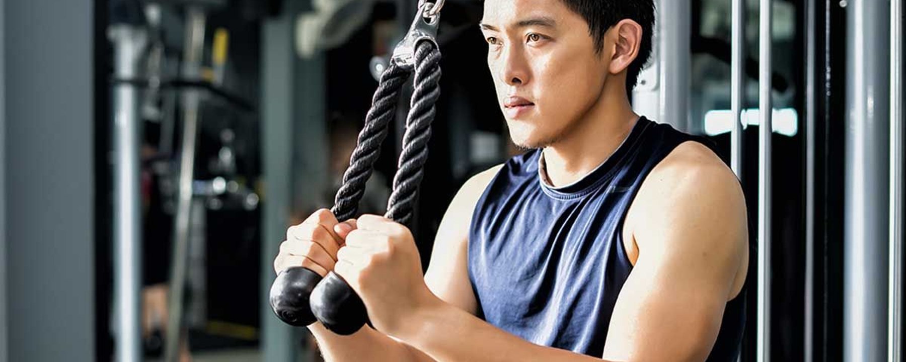 Homme en débardeur utilisant une machine à câbles pour travailler les triceps au gymnase