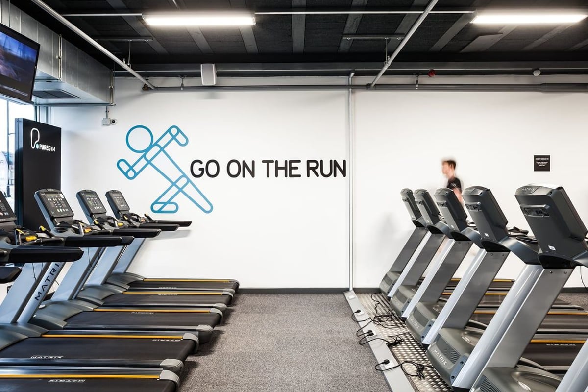 PureGym Altrincham: Rows of treadmills and text on the wall saying "Go on the run" in a gym setting.