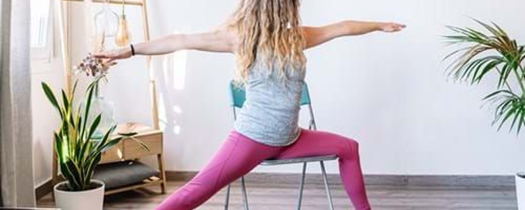 Woman in pink leggings doing yoga pose using a chair in a bright room