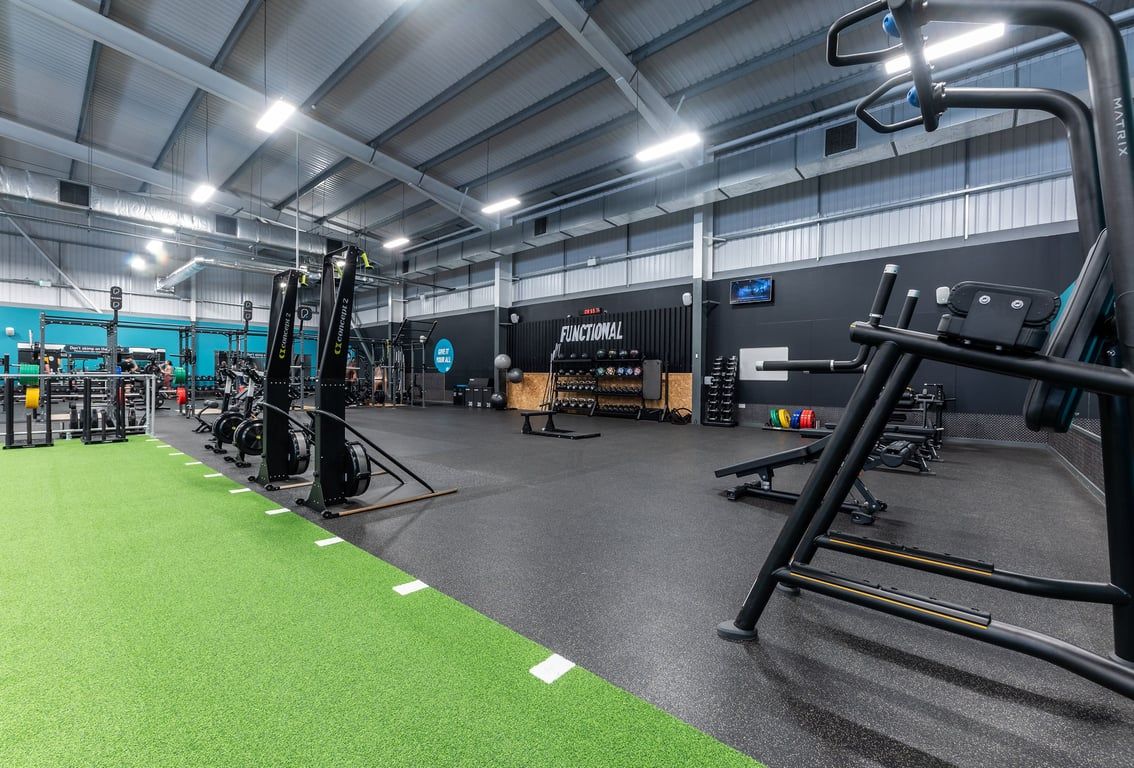 PureGym Widnes: Functional training area with green turf, squat racks, weightlifting platforms, and rubberized flooring.