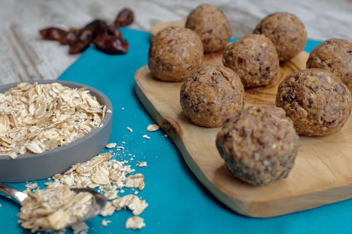 Energy balls with oats and dates on wooden board beside bowl of oats and scattered dates