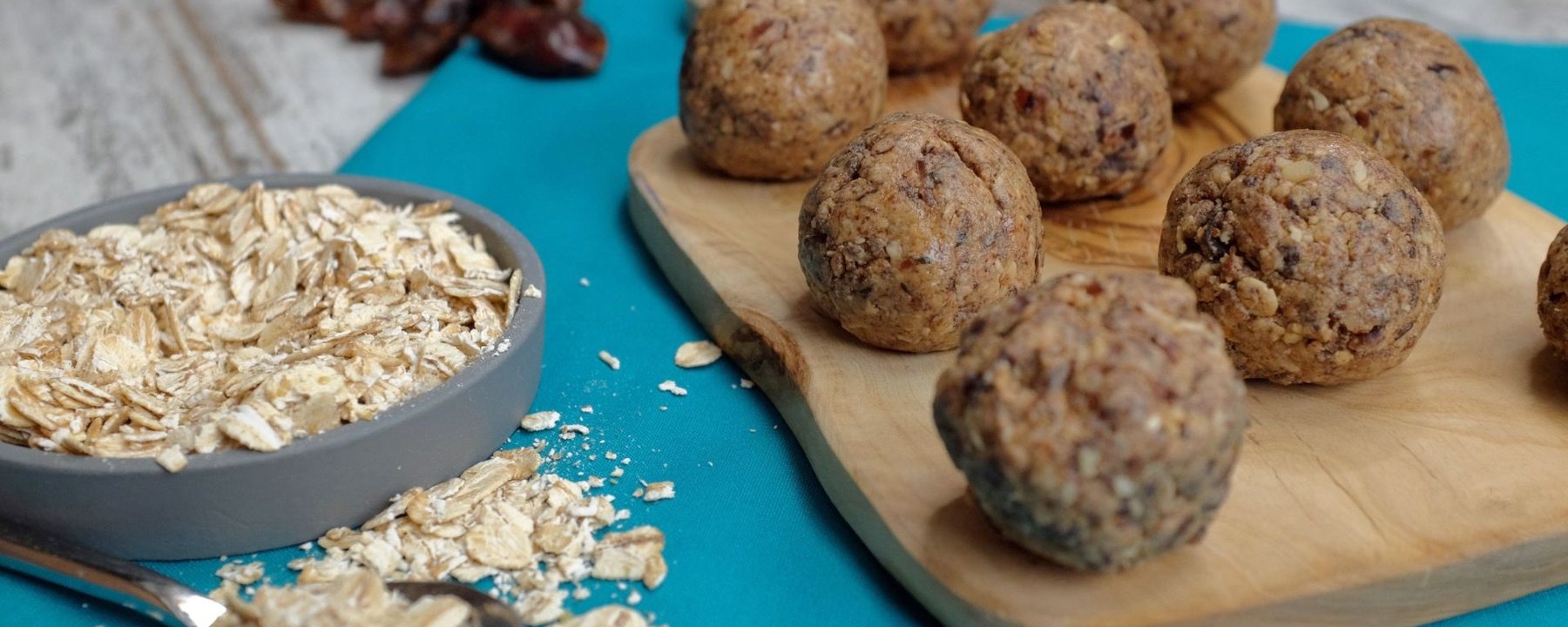 Energy balls with oats and dates on wooden board beside bowl of oats and scattered dates