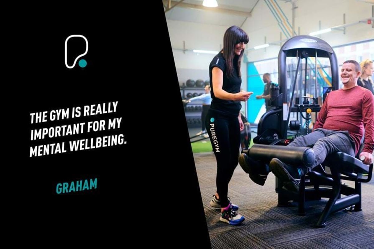 Man exercising legs on machine with female trainer smiling beside him in gym