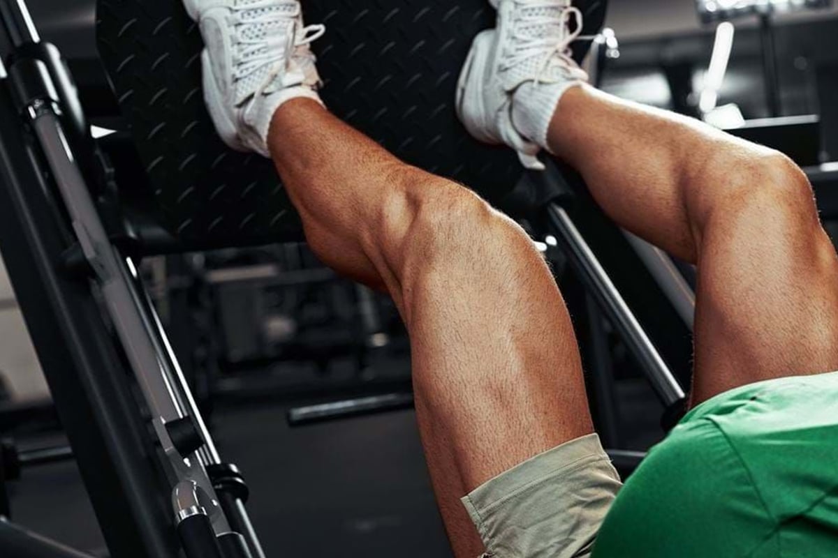 Man wearing white trainers and green shirt using leg press machine at gym