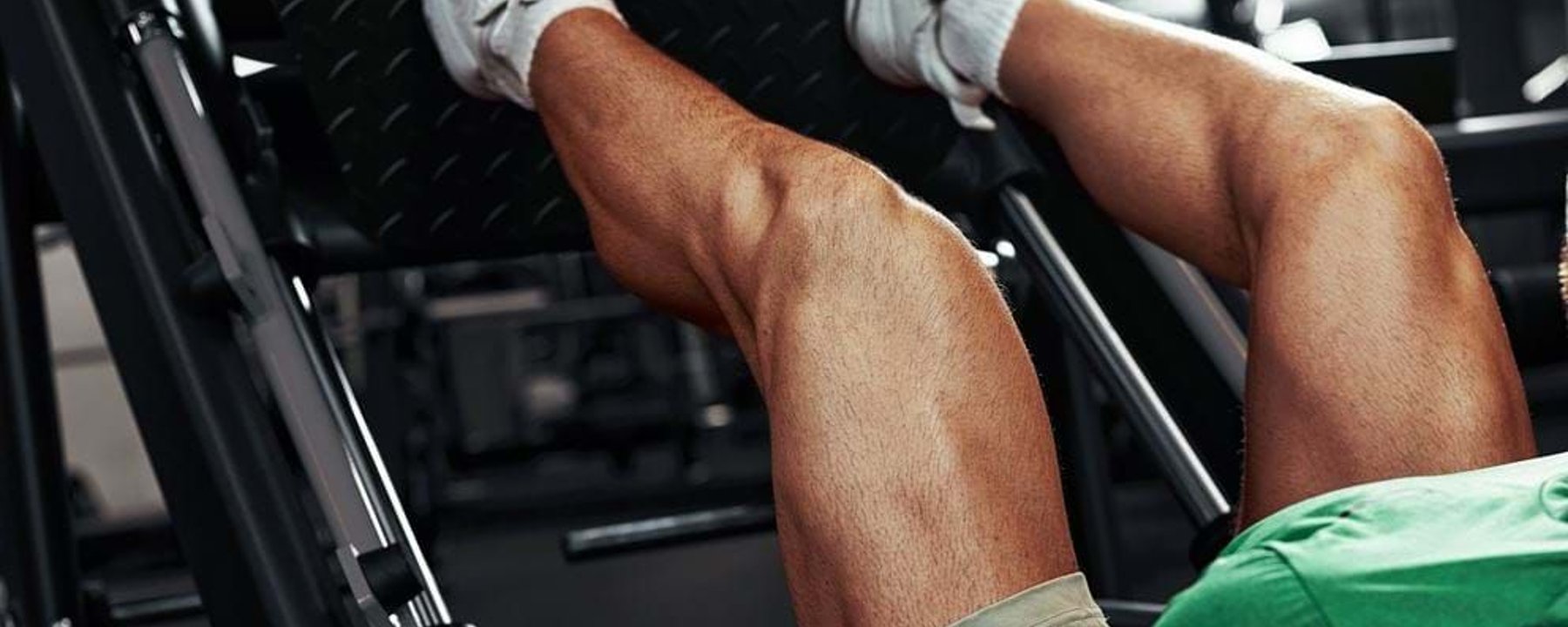 Man wearing white trainers and green shirt using leg press machine at gym