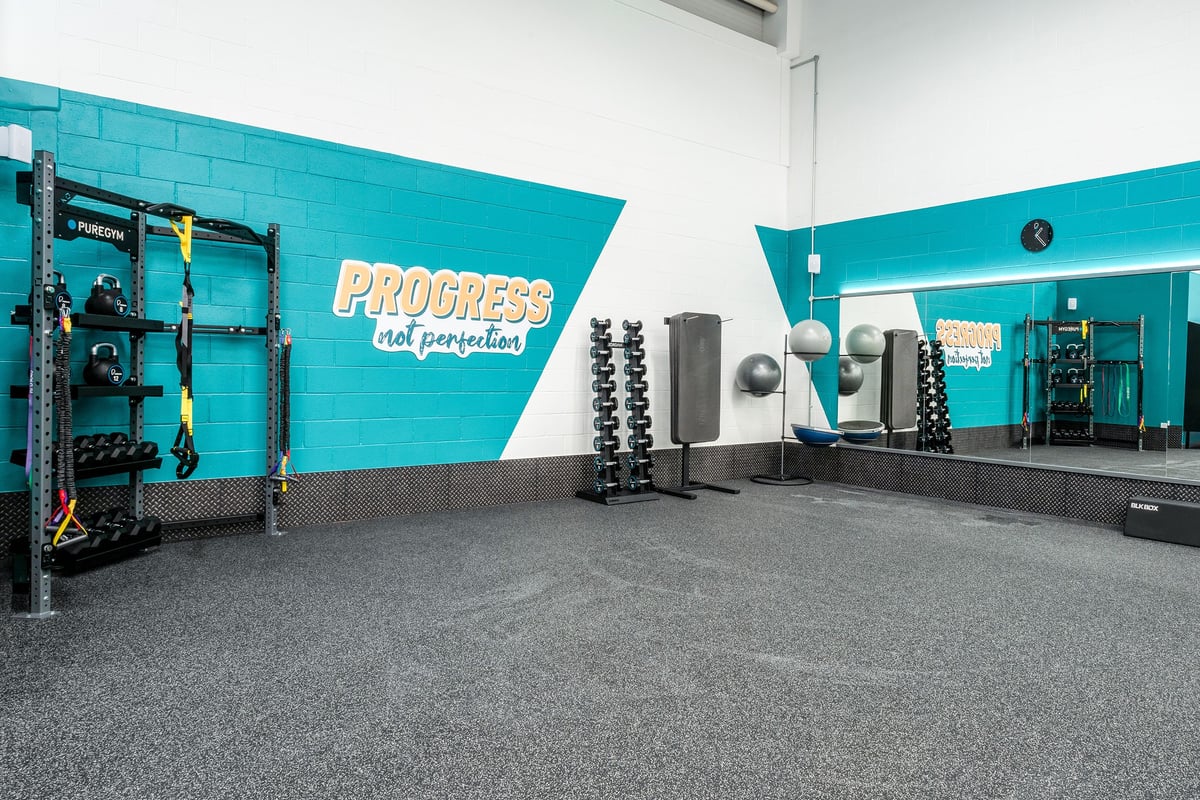 PureGym Cannock Orbital Retail Park: Squat rack, weight plates, dumbbells, rubberized flooring, and teal accent wall.