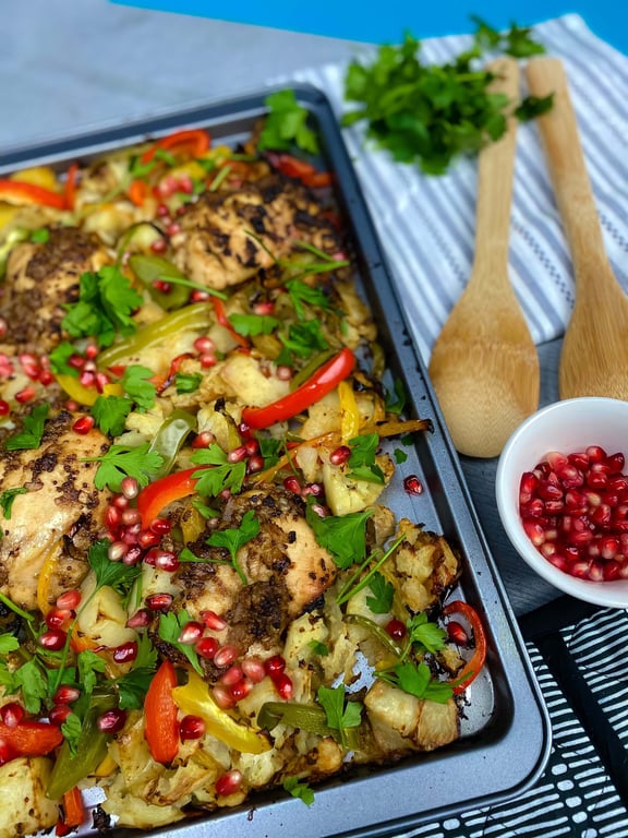 Tray of roasted chicken with mixed peppers, cauliflower, parsley, and pomegranate seeds