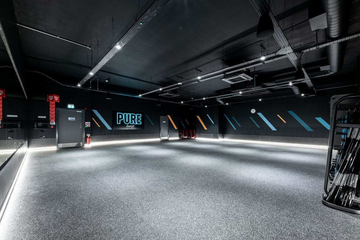 PureGym Solihull Sears Retail Park: Rubberized floor, neon lighting, exposed ducts overhead in a dark fitness studio.