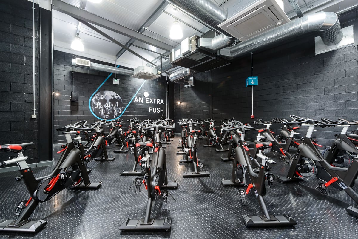PureGym Leeds Regent Street: Rows of stationary exercise bikes in a dimly lit studio with exposed ducts and brick walls.