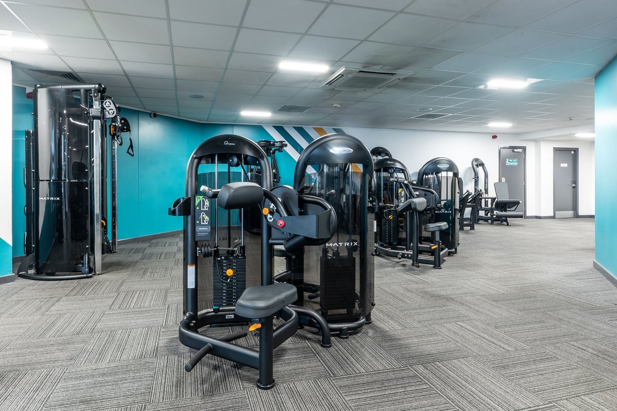 PureGym Brierley Hill: Rows of strength machines, rubberized flooring, and teal accent walls in a gym studio.