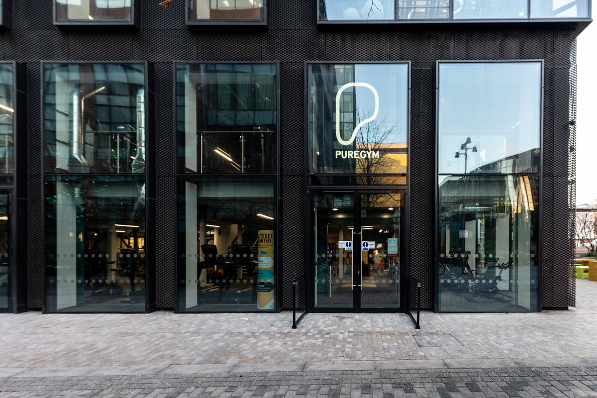 PureGym Manchester First Street: Glass storefront with PureGym logo, glimpses of gym equipment inside.